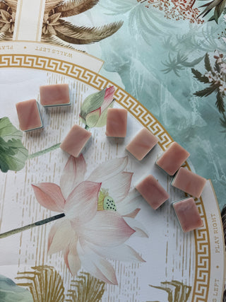 Ten Onyx Rose luxury Mahjong tiles are arranged on a decorative White Lotus Mahjong Mat from Mahj Tile Haus with a lotus flower illustration and gold border, set against a soft green botanical background.